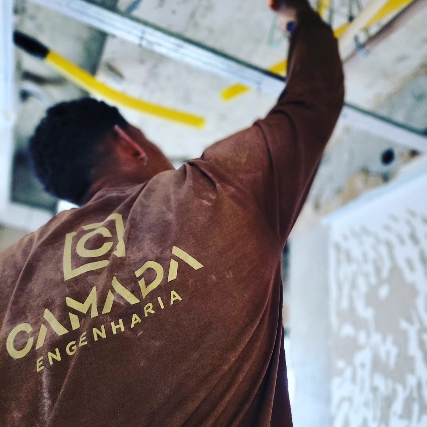 Integrante da equipe da Camada Engenharia em obra, de uniforme marrom com o logo da empresa nas costas.